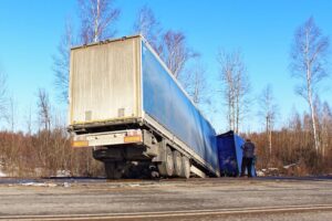 Tilted wrecked semi truck on roadside ditch on sunny spring day, suburban highway road accident